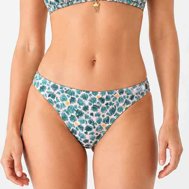 Mujer con braguita de bikini de corte clásico entera con estampado de hojas de palmera verdes y detalles amarillos sobre fondo rosa.