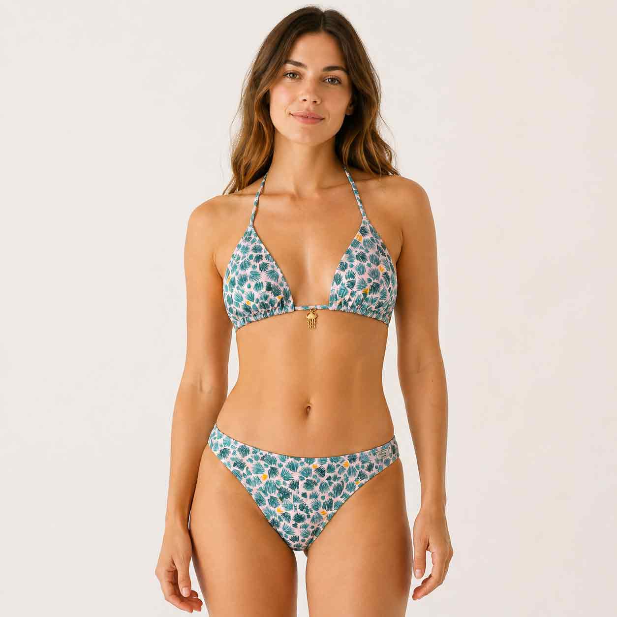 Chica con un top de bikini de triángulo con estampado de palmeras verdes y detalle de colgante dorado en el centro.
