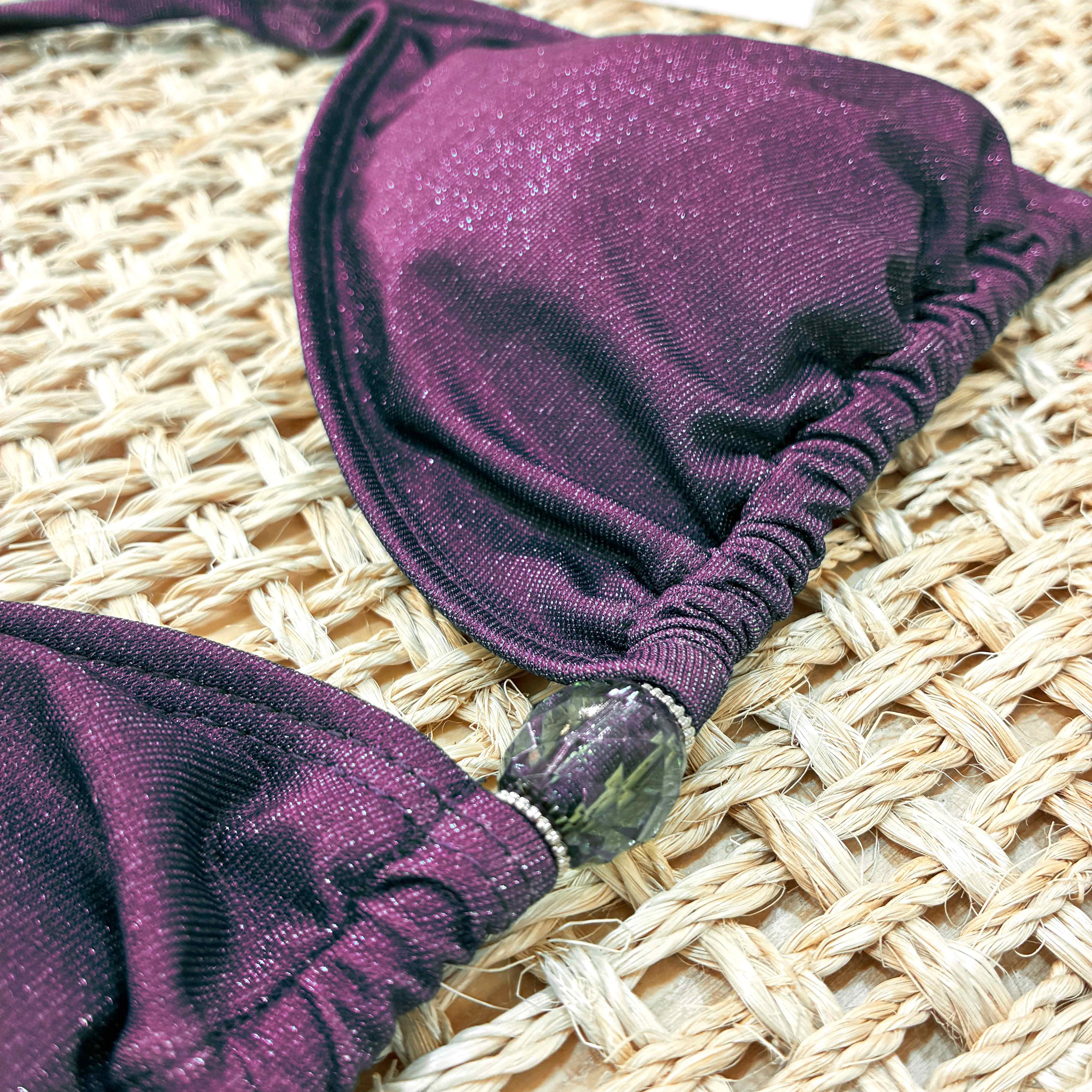 Detalle de adorno de un  op de bikini artesanal modelo triángulo cortina en tejido lurex brillante color berenjena. 