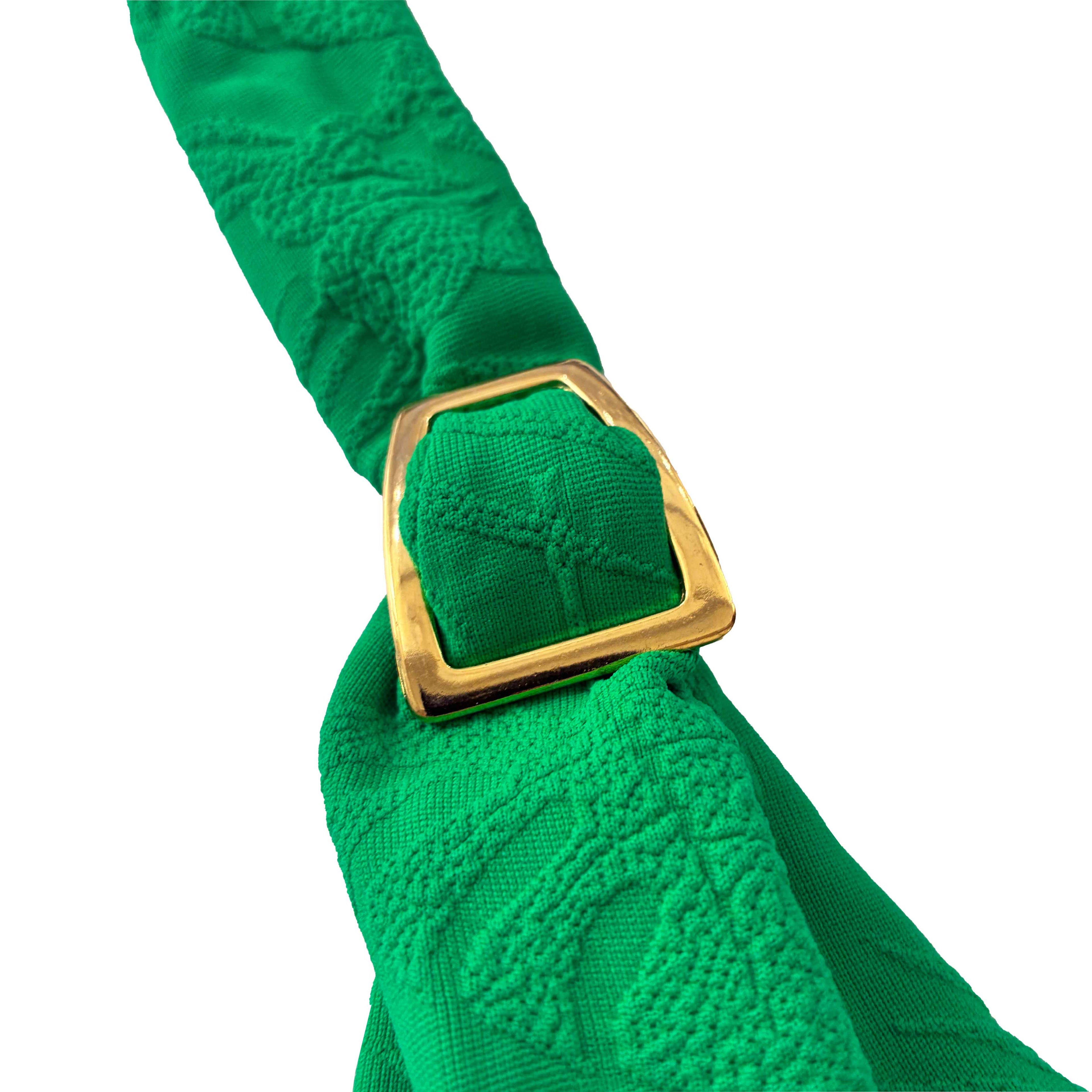 Primer plano de hebilla metálica dorada en el tirante de un bikini verde esmeralda con tejido de palmeras en relieve.
