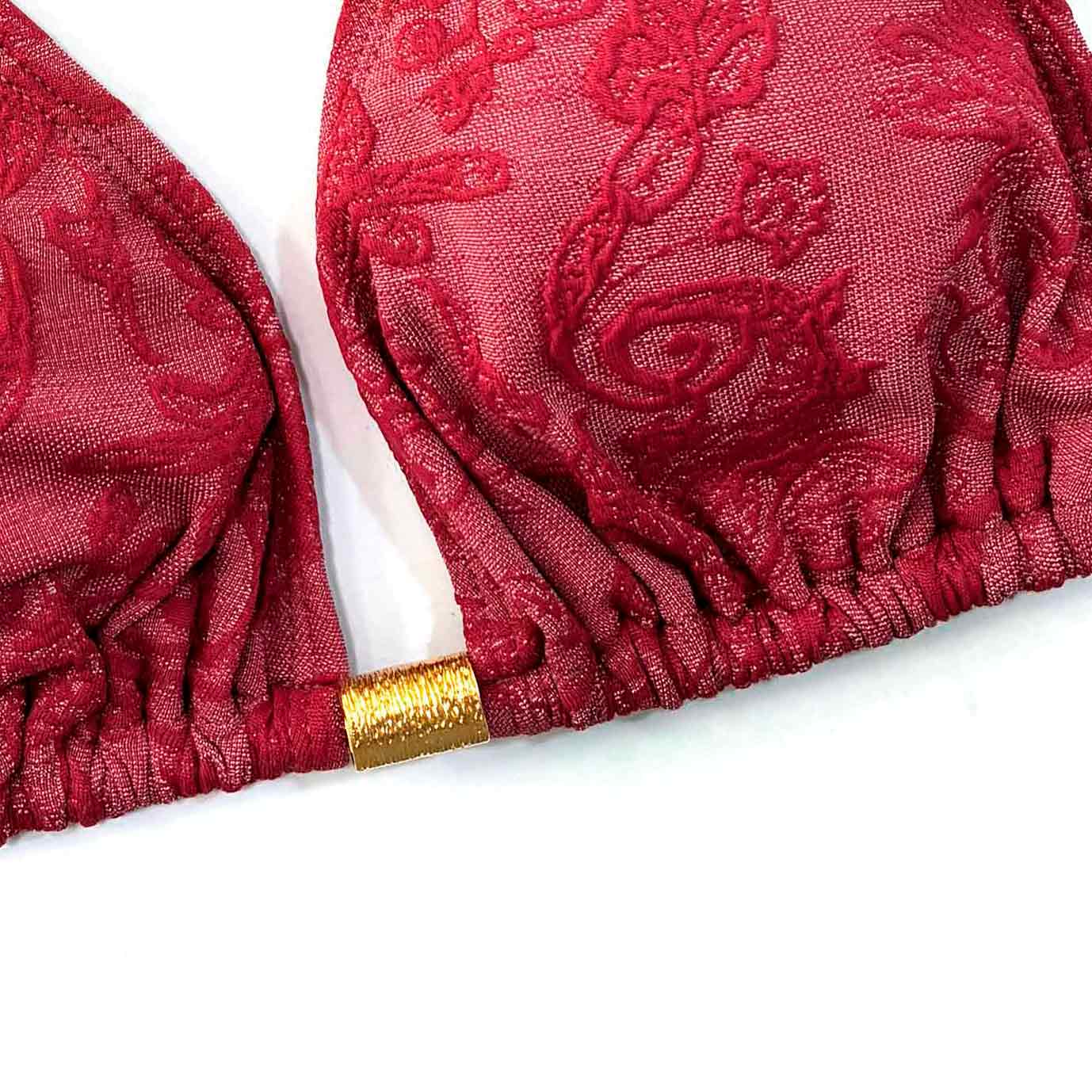 Top de bikini de triángulo alto en color burdeos con textura adamascado floral y lazos de sujeción anudados, con detalle dorado central de Moh,S.