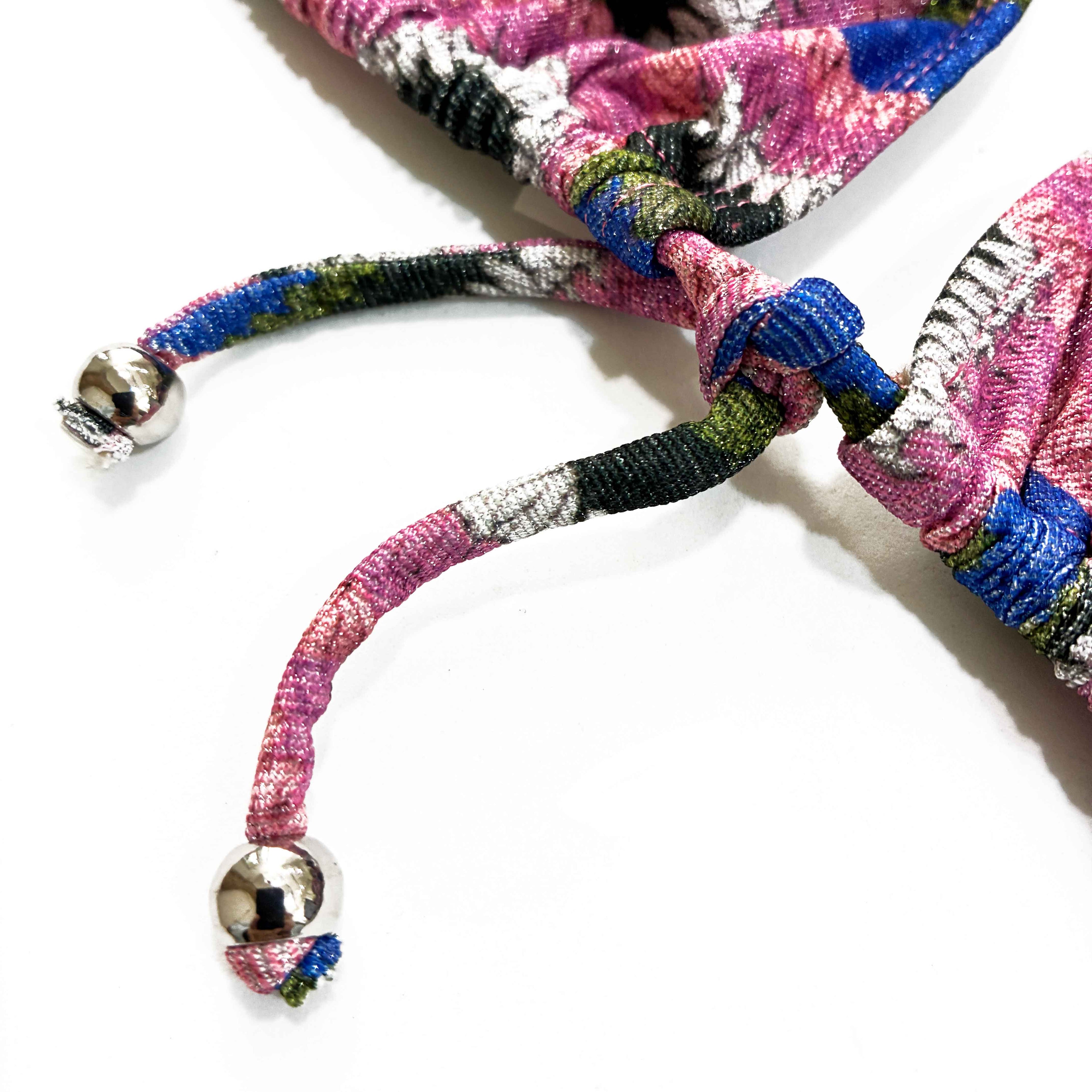 Detalle de adorno metálico de top de bikini de lurex brillante con estampado estilo crochet artesanal en tonos rosa, azul y verde.