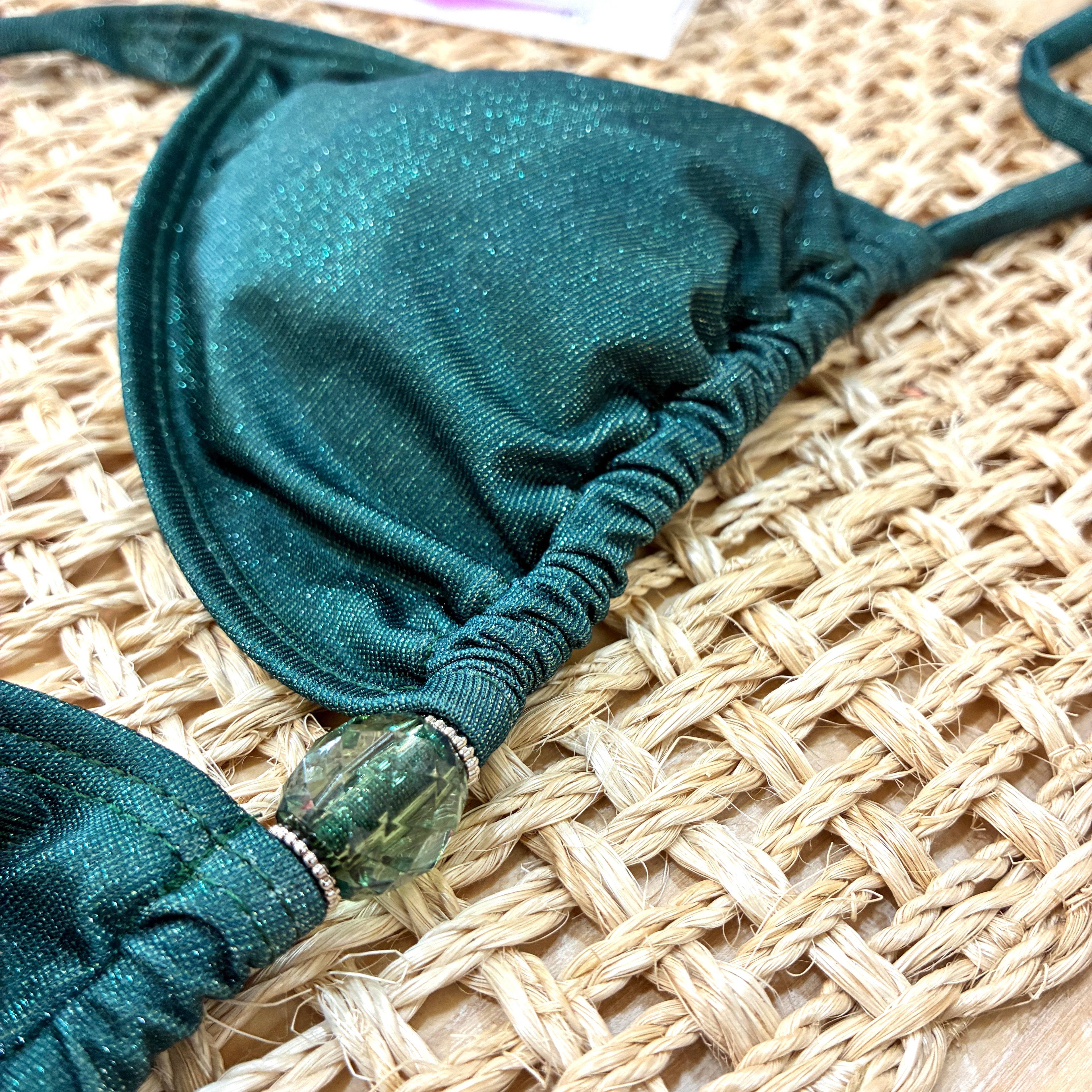 Detalle de adorno de top de bikini tipo triángulo cortina en color verde esmeralda brillante con detalle de cuenta central, hecho a mano.