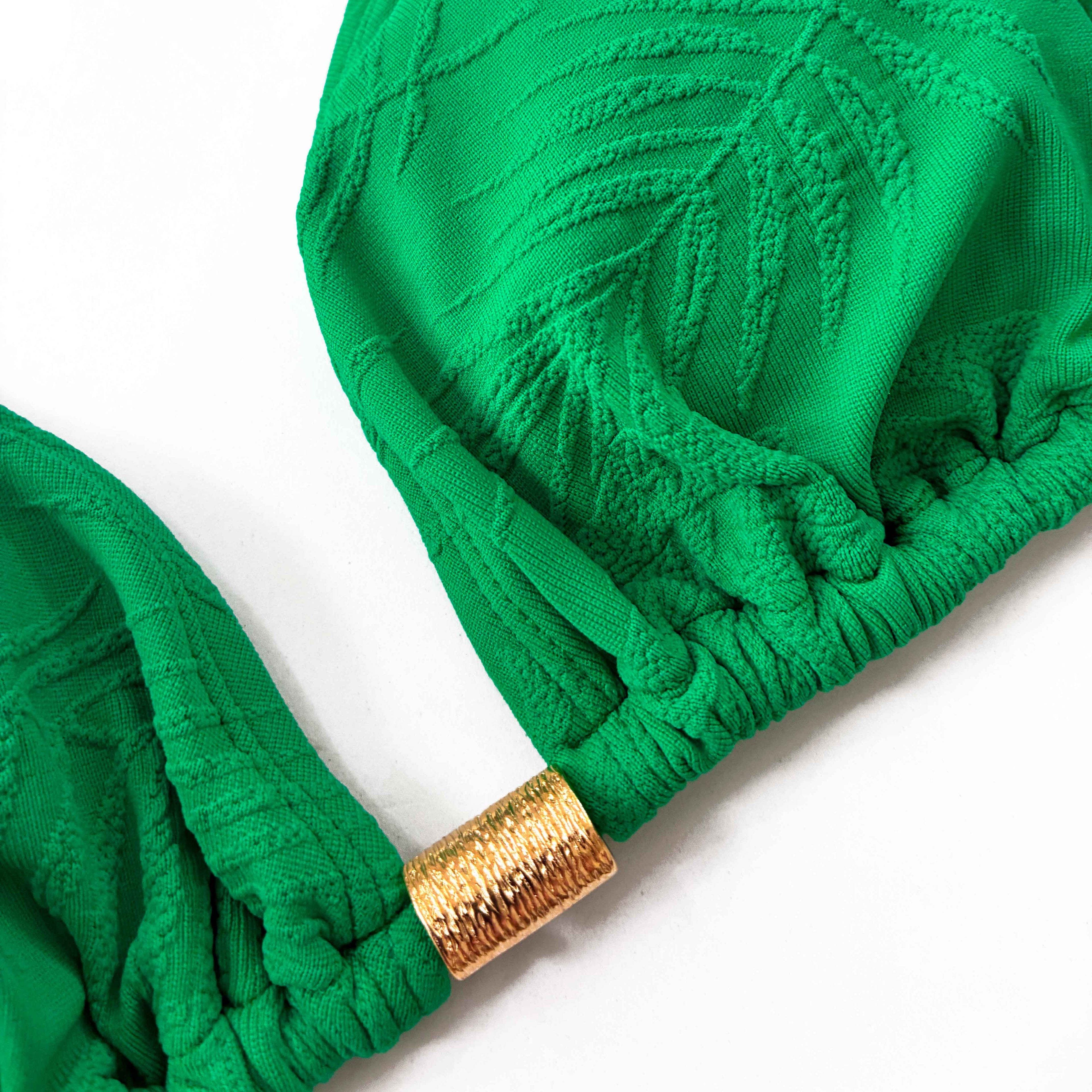 Detalle de pieza dorada central de top de bikini de triángulo cortina en color verde esmeralda con tejido texturizado de palmeras.