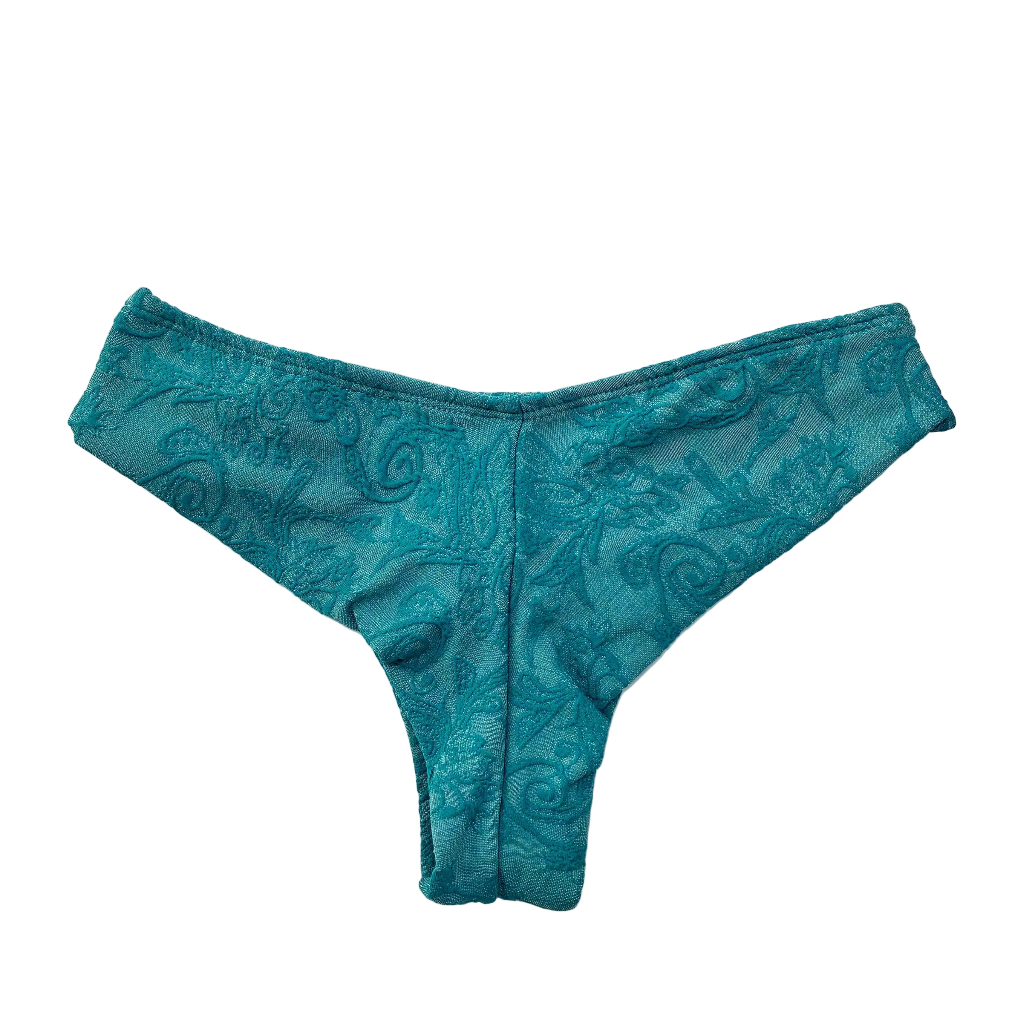 Vista trasera de braga de bikini semitanga verde esmeralda con relieve adamascado, fabricada artesanalmente en Tarifa en edición limitada, mostrando el corte que realza el trasero.